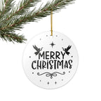 Front view of White ceramic Christmas ornament with graphic displaying stars, angels, and text that says Merry Christmas hanging on a tree branch