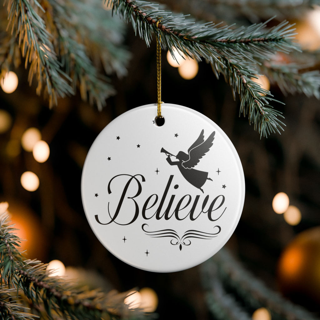 Front view of White ceramic Christmas ornament with graphic displaying stars, an angel, and text that says Believe. Hanging in a tree
