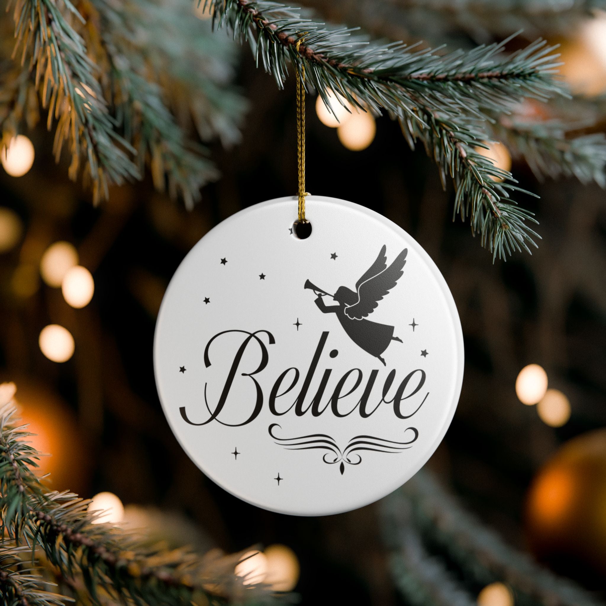 Front view of White ceramic Christmas ornament with graphic displaying stars, an angel, and text that says Believe. Hanging in a tree