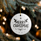 Front view of White ceramic Christmas ornament with graphic displaying stars, angels, and text that says Merry Christmas hanging in a tree