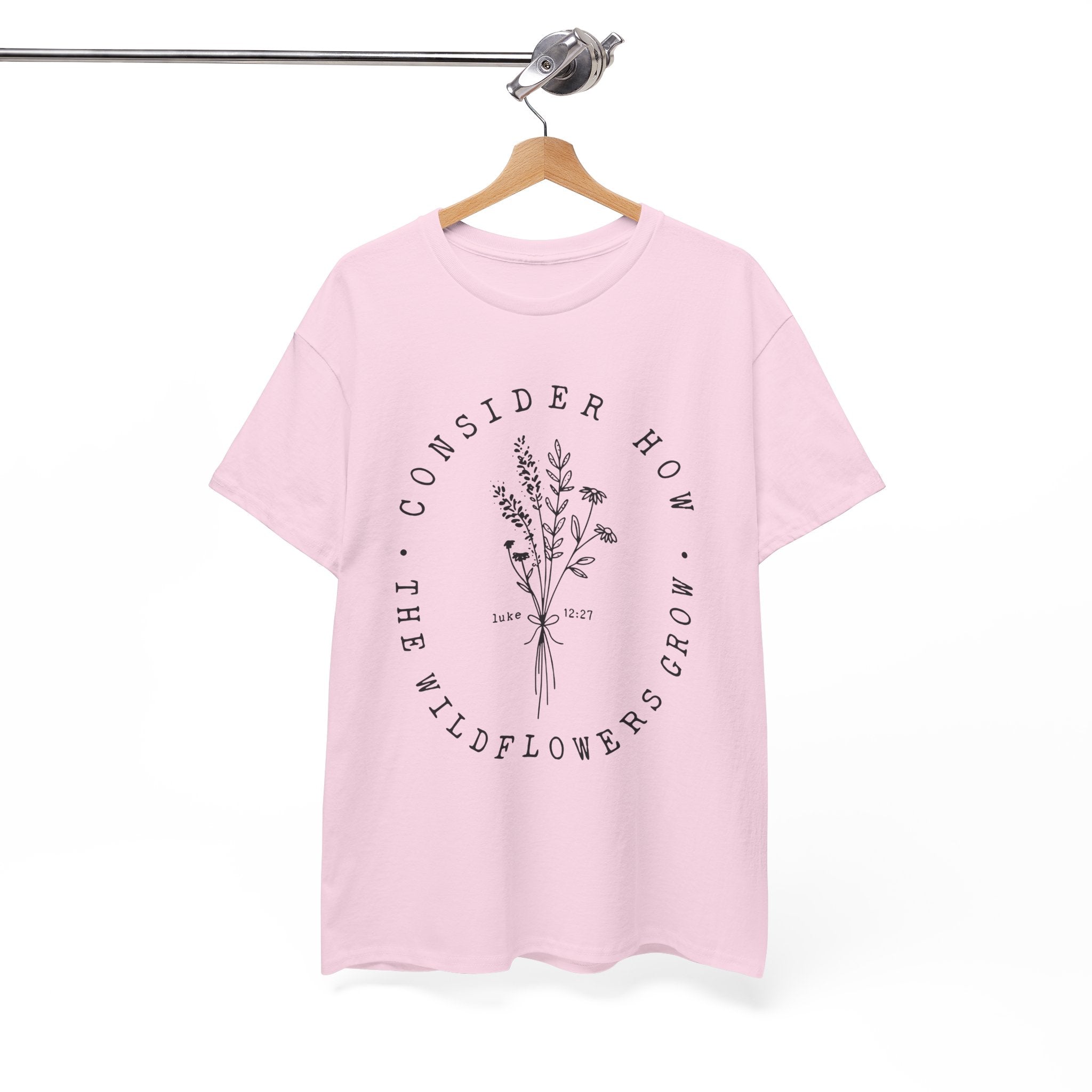 Front view Light Pink t-shirt with large black floral graphic and Luke 12:27 Bible verse displayed on a hanger