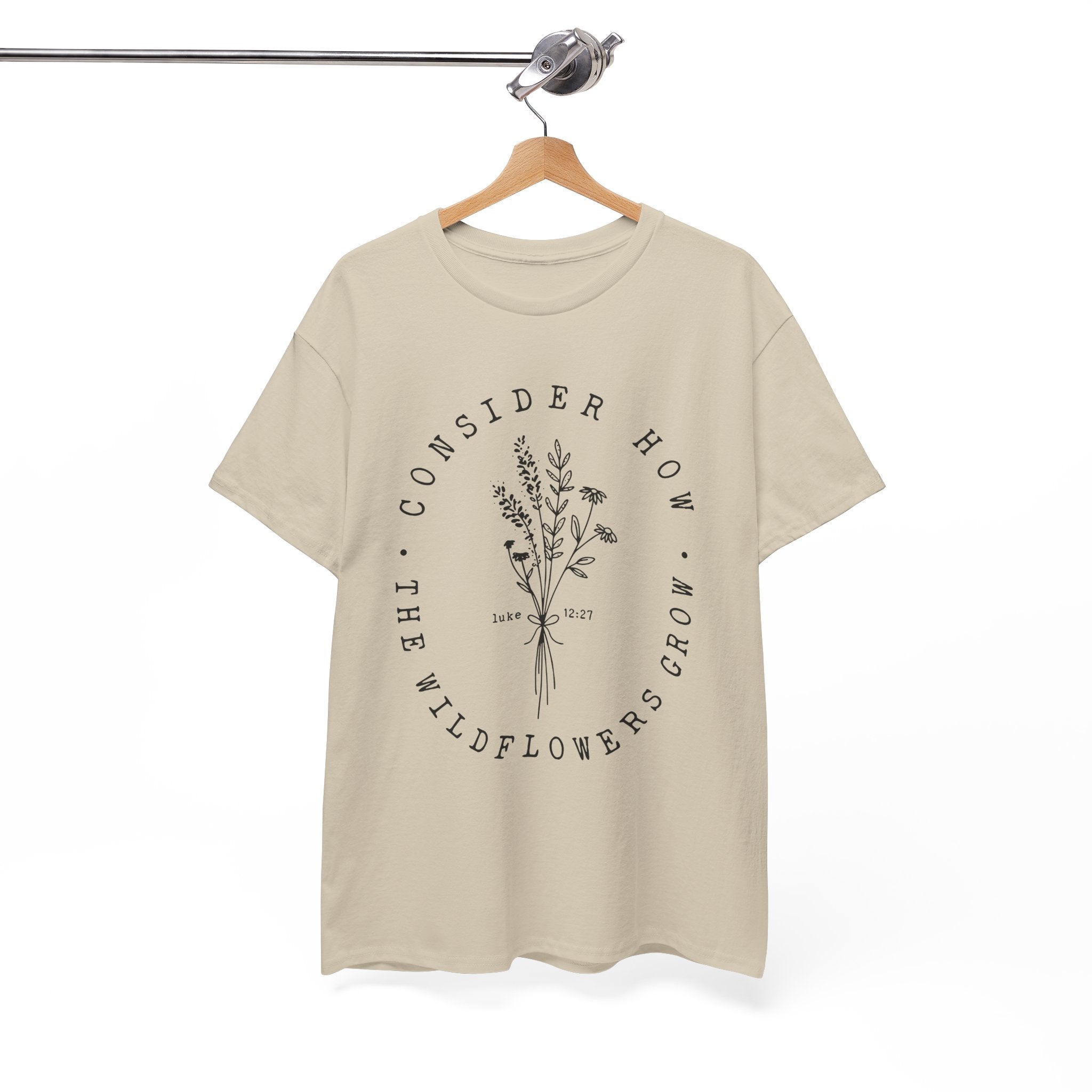 Front view Sand t-shirt with large black floral graphic and Luke 12:27 Bible verse displayed on a hanger