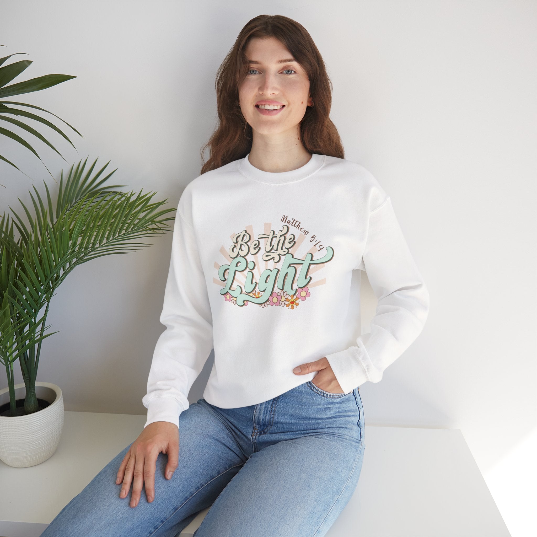 Front view White crewneck sweatshirt colorful graphic and text saying ‘Be the Light’ displayed on a model