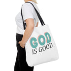 Front view of large White tote bag with black handles, colorful graphic that says God is Good, displayed over model’s shoulder