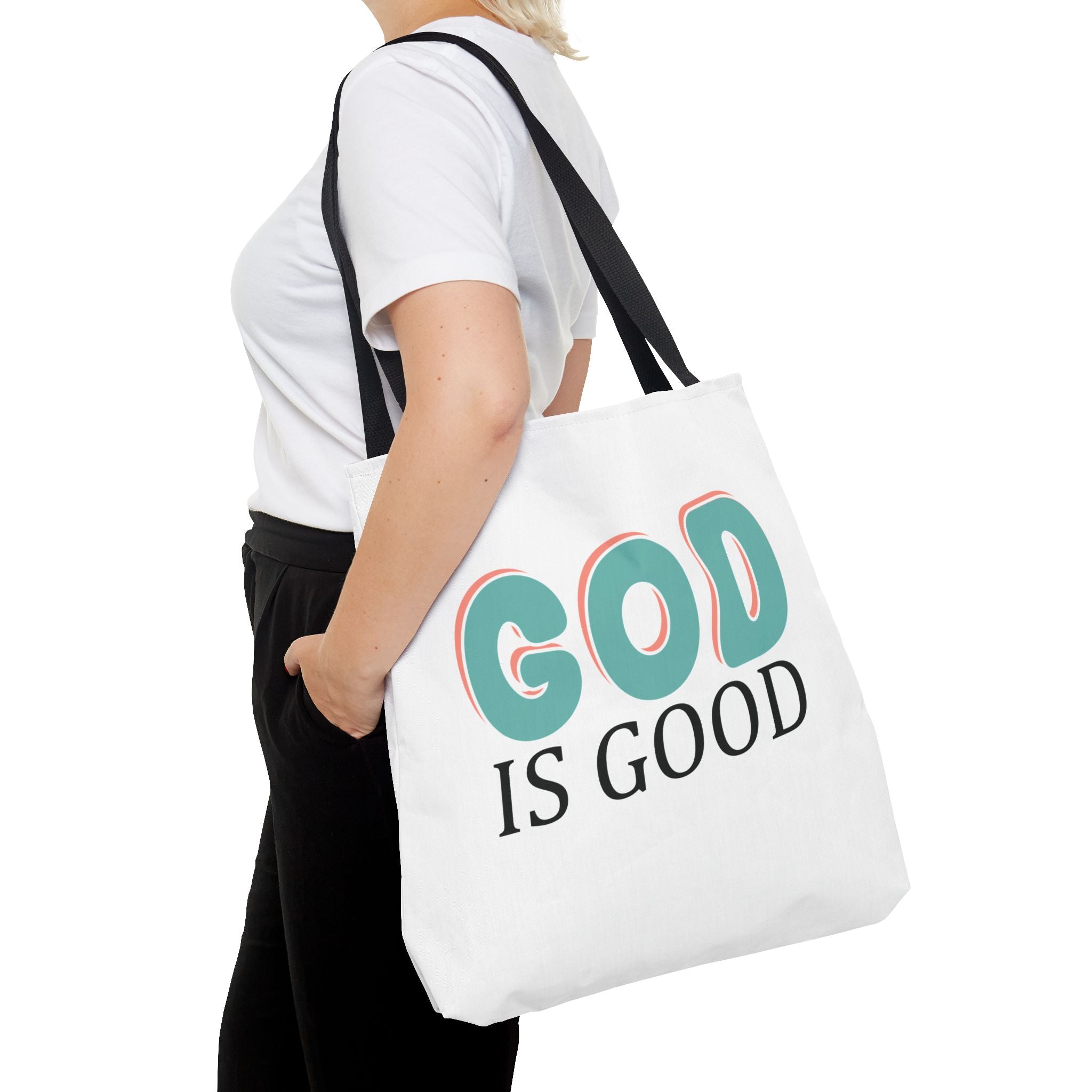 Front view of large White tote bag with black handles, colorful graphic that says God is Good, displayed over model’s shoulder