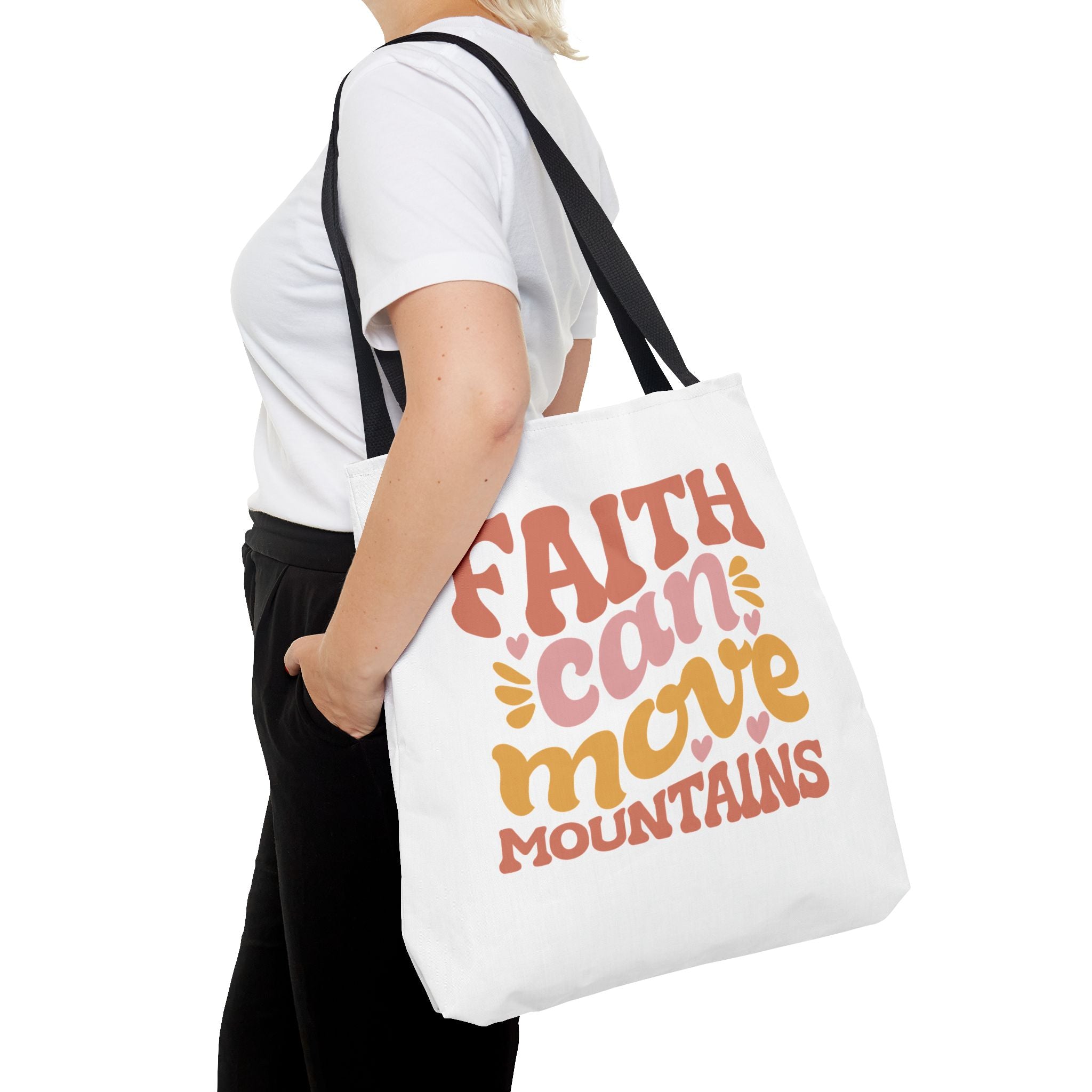 Front view of large White tote bag with black handles, colorful graphic that says Faith Can Move Mountains, displayed over model’s shoulder