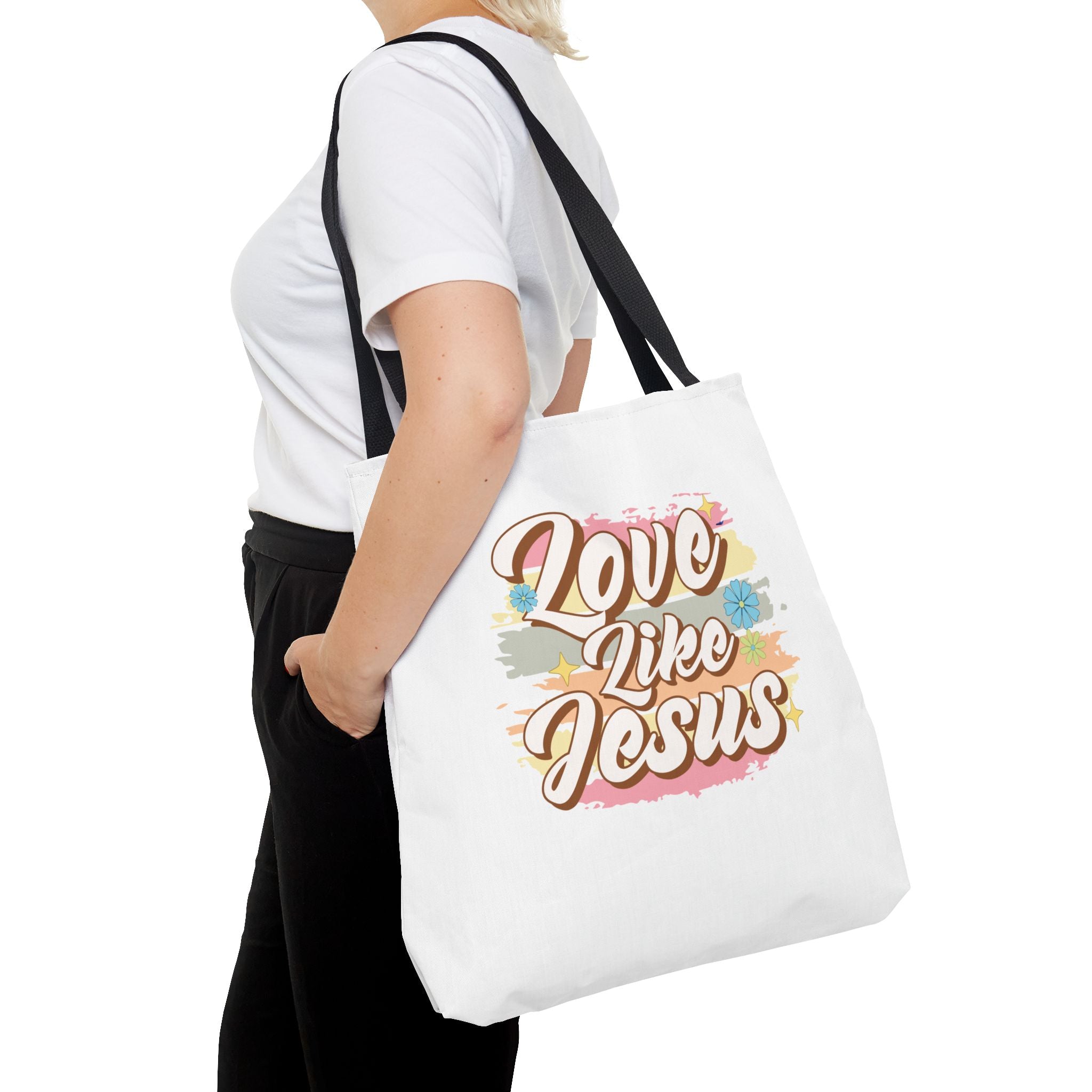 Front view of large White tote bag with black handles, colorful graphic with text Love Like Jesus, displayed over model’s shoulder