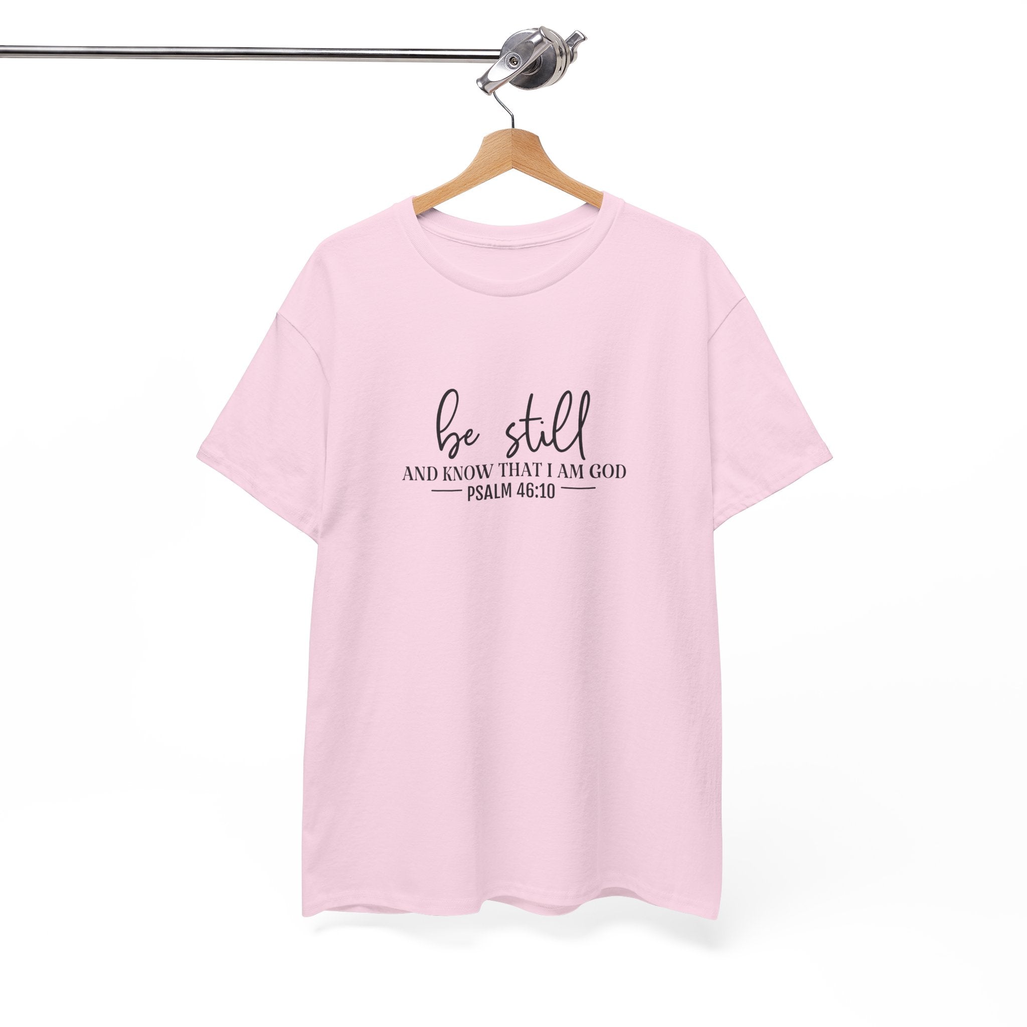 Front view of Light Pink t-shirt with black text Be Still And Know That I Am God Psalm 46:10 centered on chest. Shirt is displayed on a hanger.