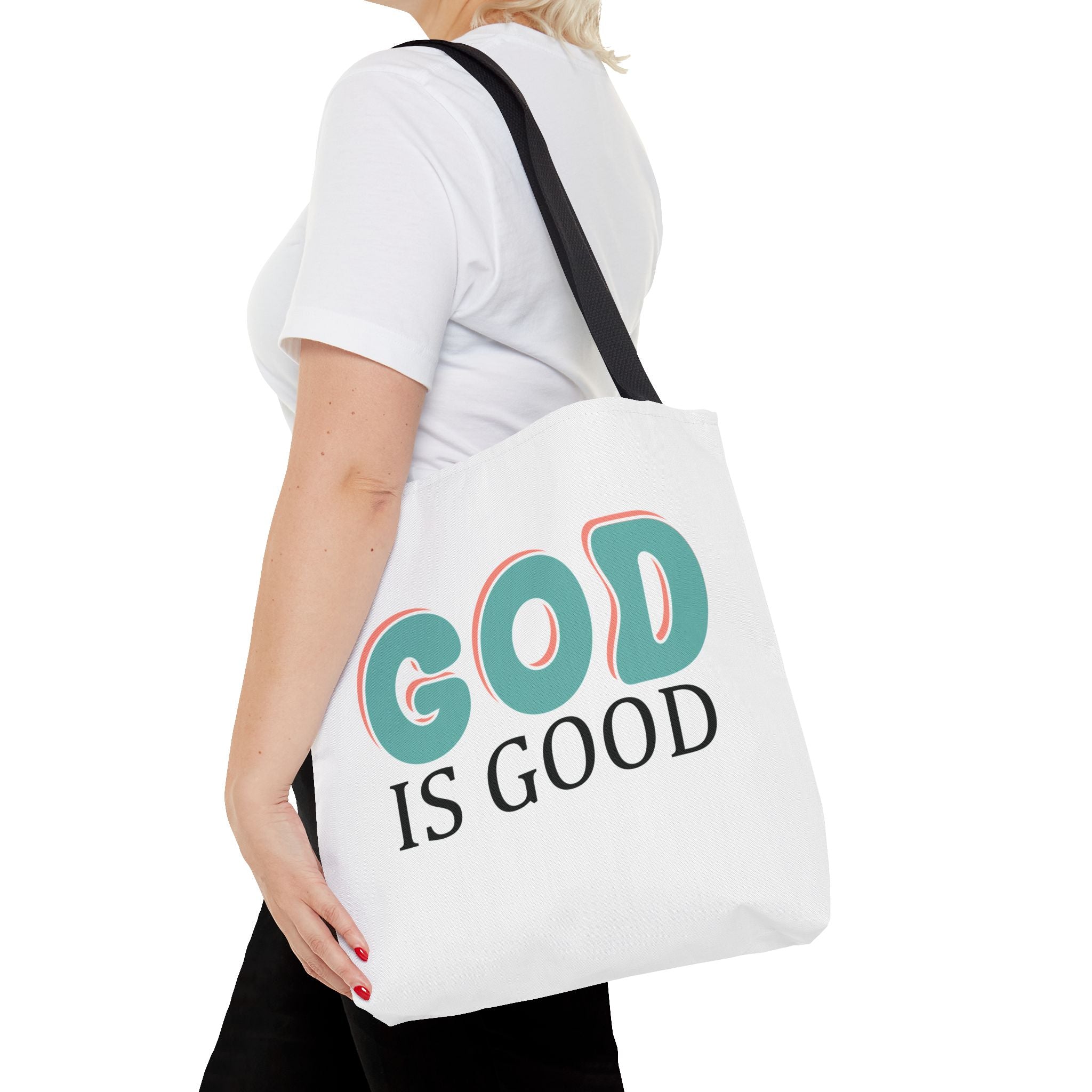 Front view of medium White tote bag with black handles, colorful graphic that says God is Good, displayed over model’s shoulder