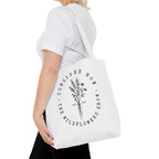 Front view of medium White tote bag with White handles, large black floral graphic and Luke 12:27 Bible verse, shown on model's shoulder