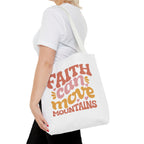 Front view of medium White tote bag with white handles, colorful graphic that says Faith Can Move Mountains, displayed over model’s shoulder