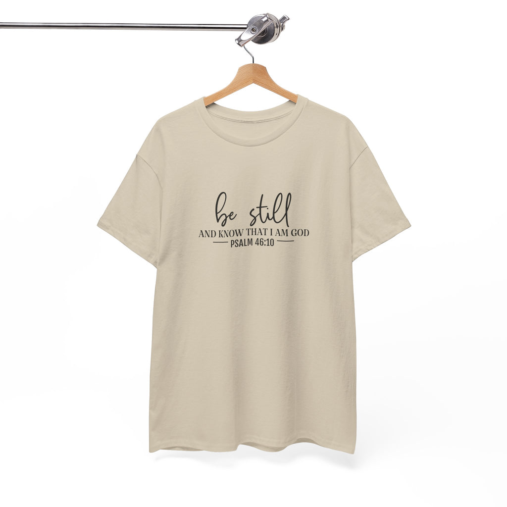 Front view of Sand t-shirt with black text Be Still And Know That I Am God Psalm 46:10 centered on chest. Shirt is displayed on a hanger.