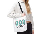 Front view of small White tote bag with black handles, colorful graphic that says God is Good, displayed over model’s shoulder
