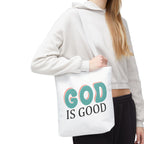 Front view of small White tote bag with white handles, colorful graphic that says God is Good, displayed over model’s shoulder