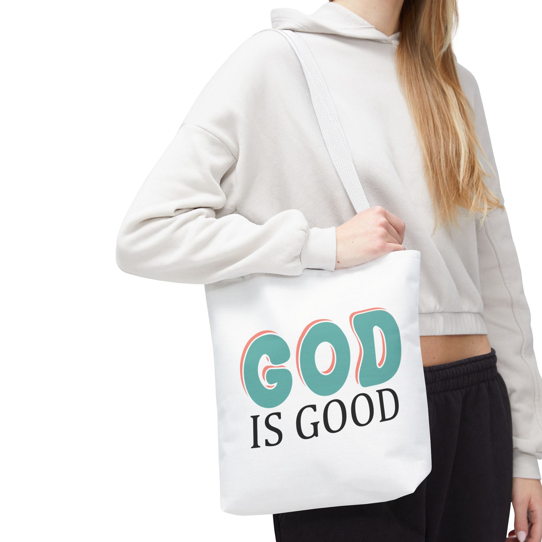 Front view of small White tote bag with white handles, colorful graphic that says God is Good, displayed over model’s shoulder