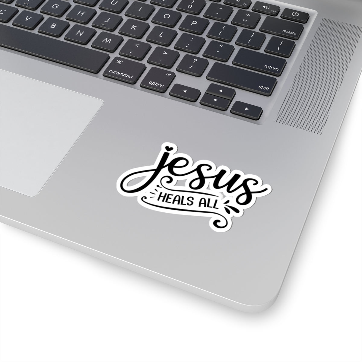 Sticker with black text saying Jesus Heals All. Displayed on laptop.