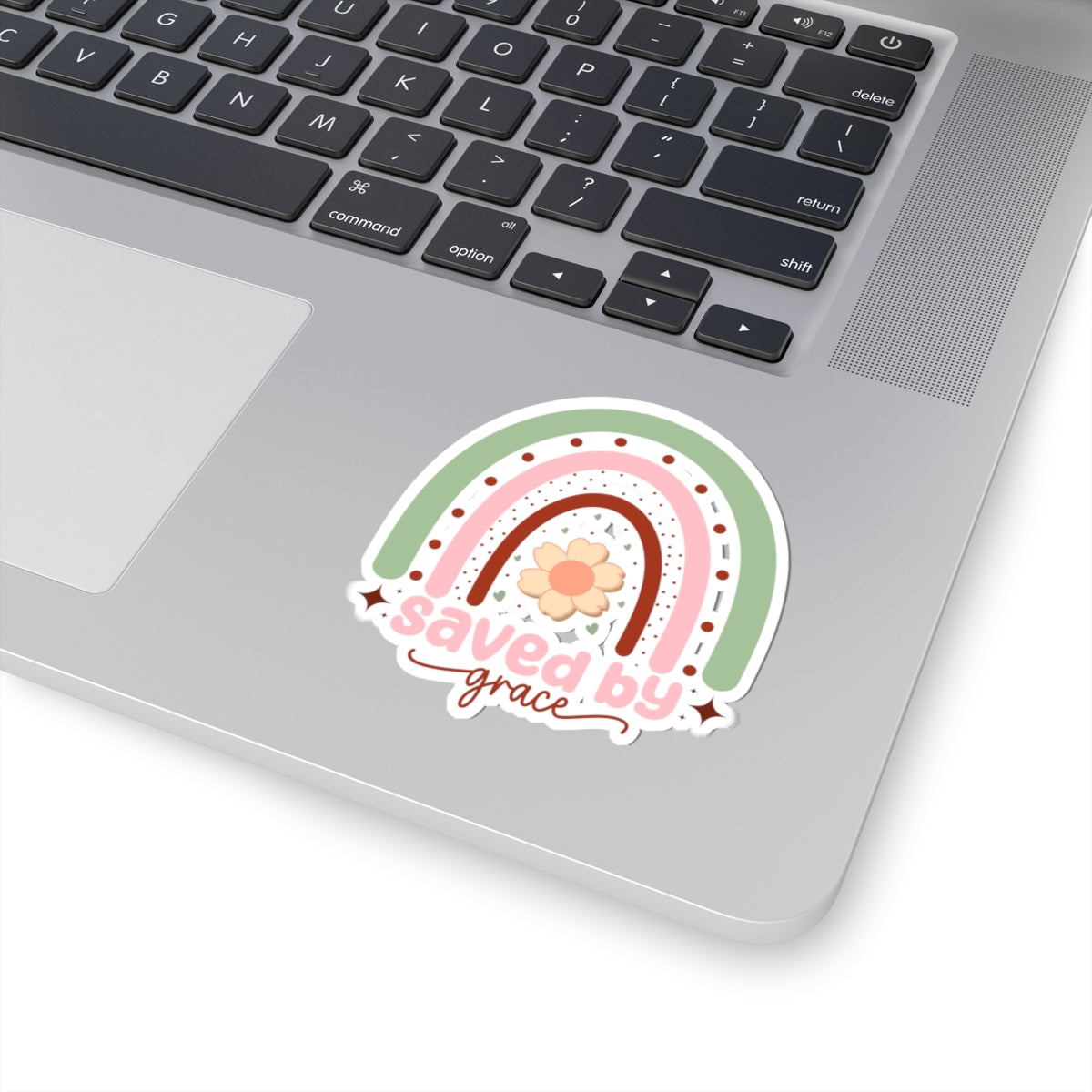 Sticker with pastel colored rainbow graphic with the text Saved by Grace. Displayed on laptop.