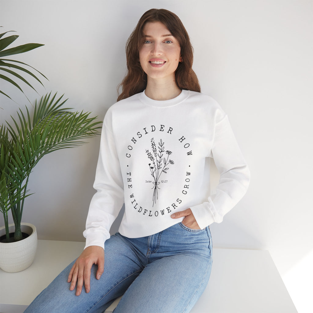 Front view White crewneck sweatshirt black floral graphic and 'Consider How the Wildflowers Grow' text from Bible verse Luke 12:27. Displayed on a model.